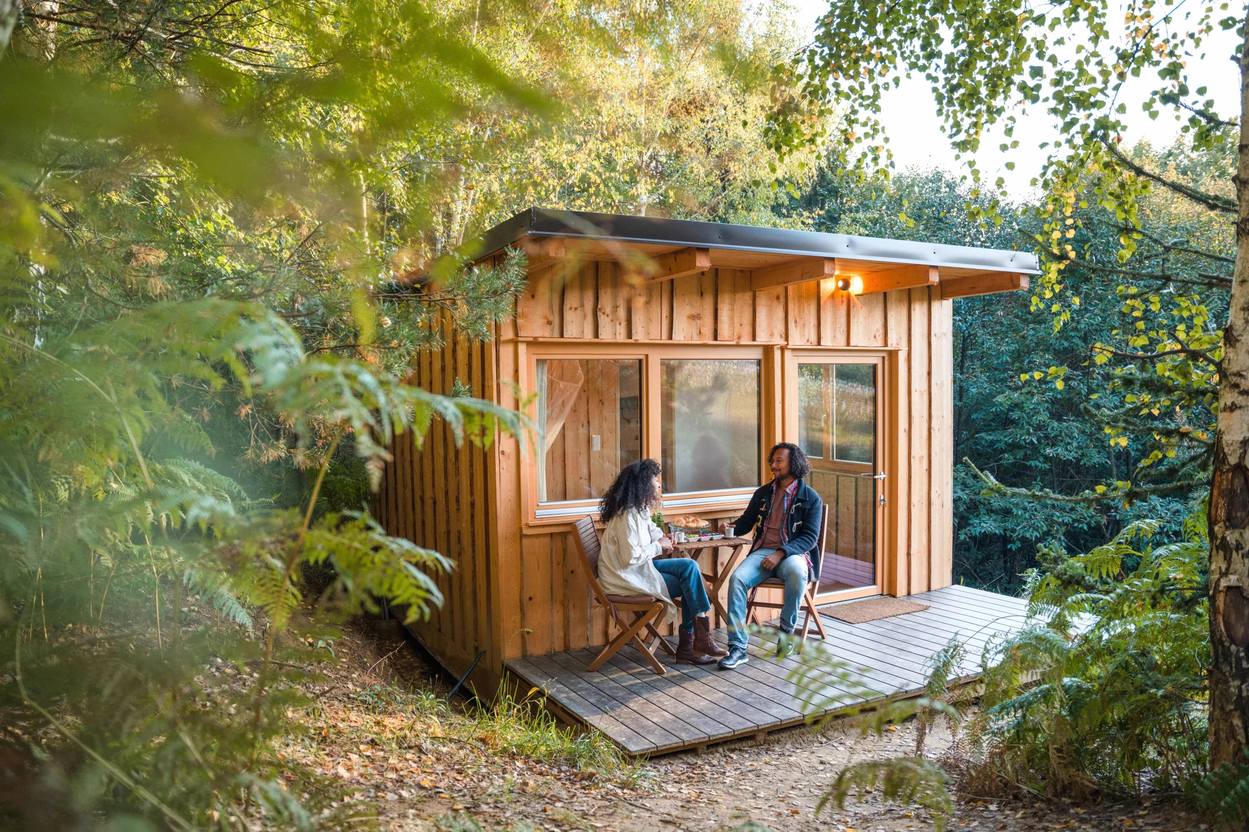 Zwei Personen sitzen vor einem Tiny House in der Natur